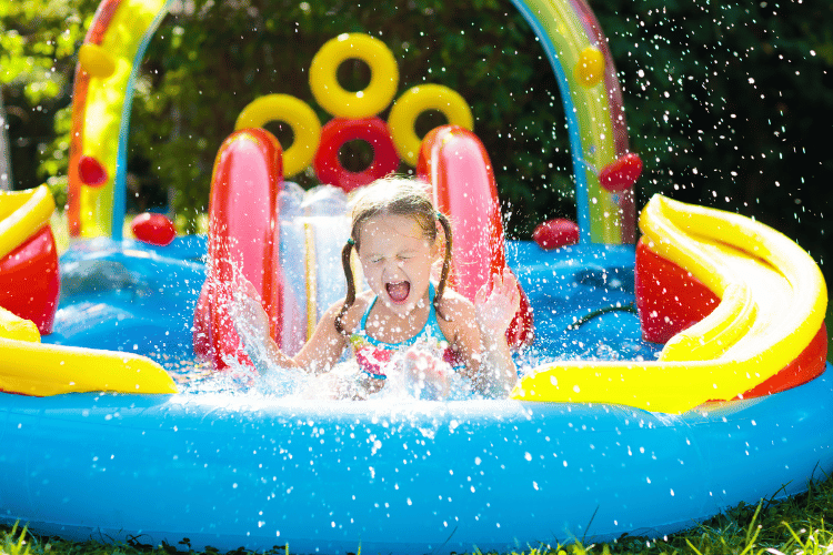 Child in garden swimming pool with inflatable water slide