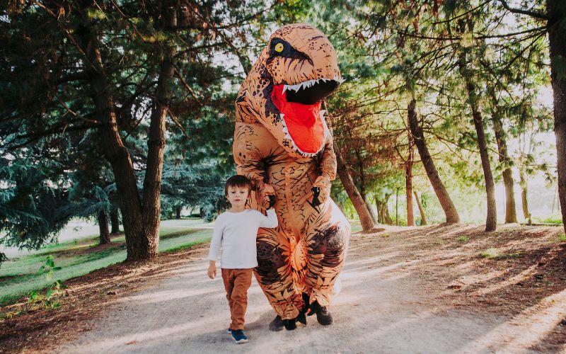 Father wearing a dinosaur costume with son waking at the park