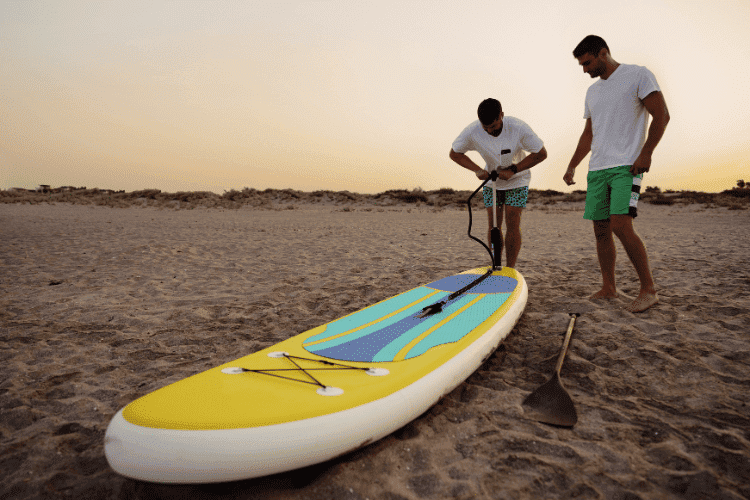 Young man inflating paddle sup board on the beach at sunrise