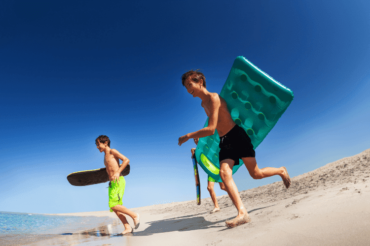Young surfers running with bodyboards along beach