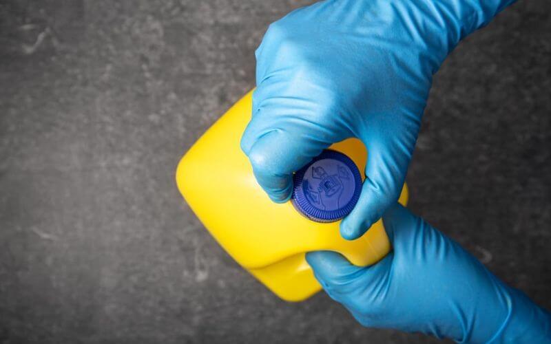 Human hand in protective glove opening a yellow bleach bottle