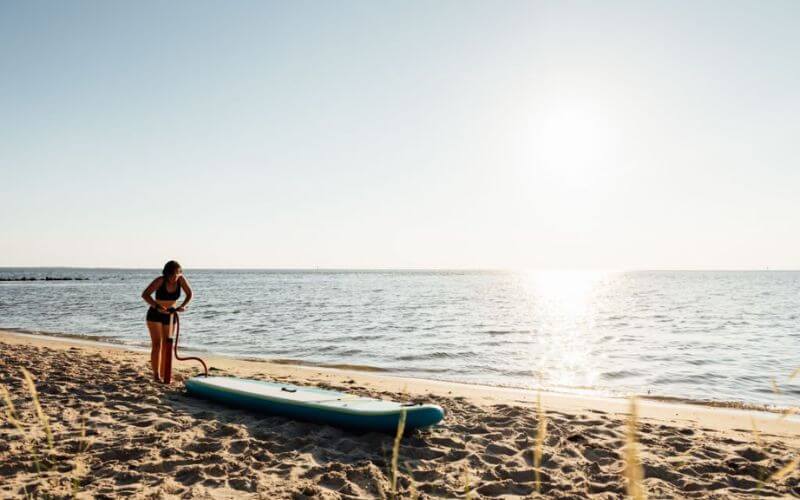 a girl inflating an inflatable paddle board under the sun