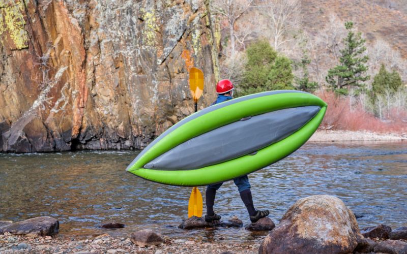 man carrying a whitewater inflatable kayak